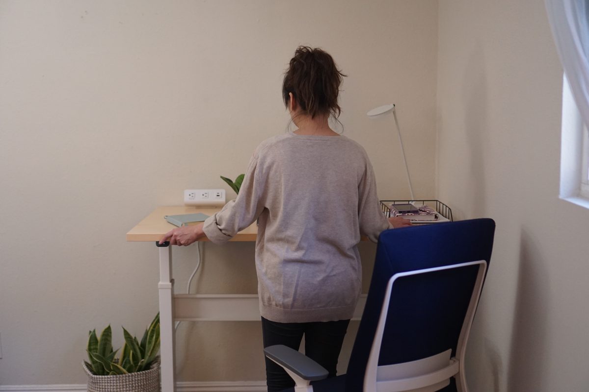 A woman standing at the raised Bonita ET desk in the corner of a den, one hand on the front edge