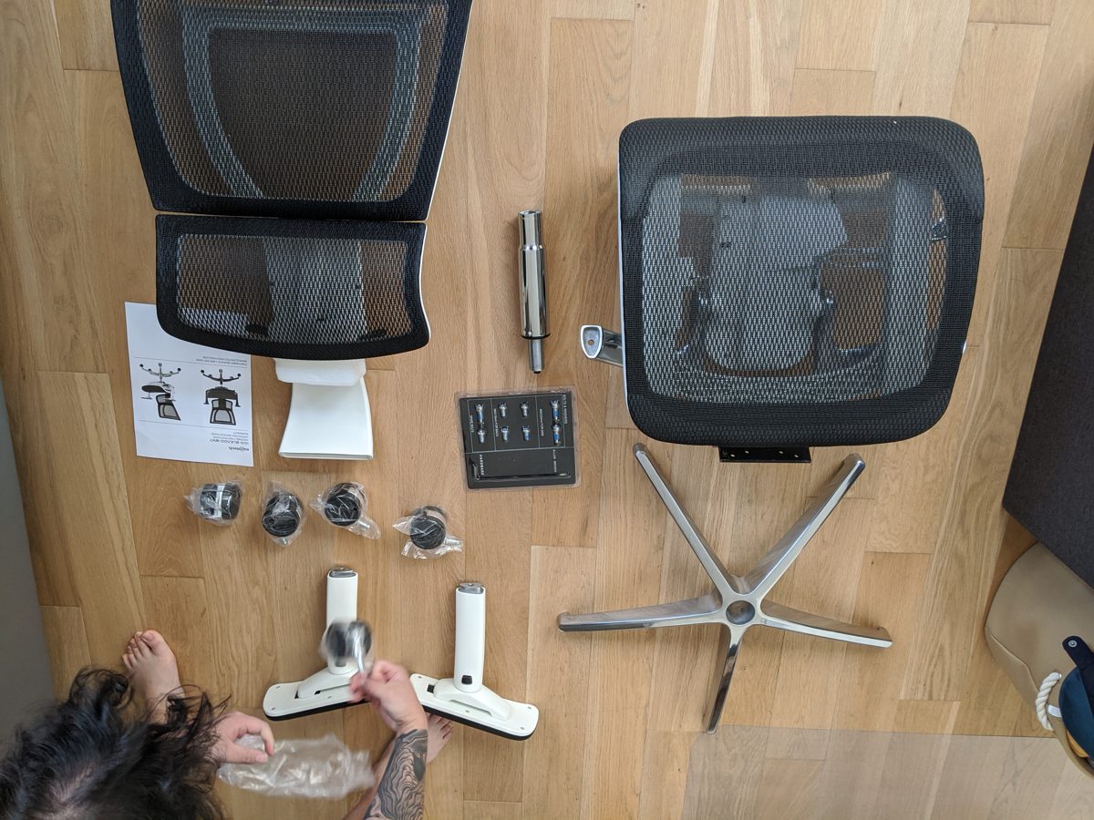Eurotech iOO parts laid out on a wood floor from above, with my hands working on the armrests