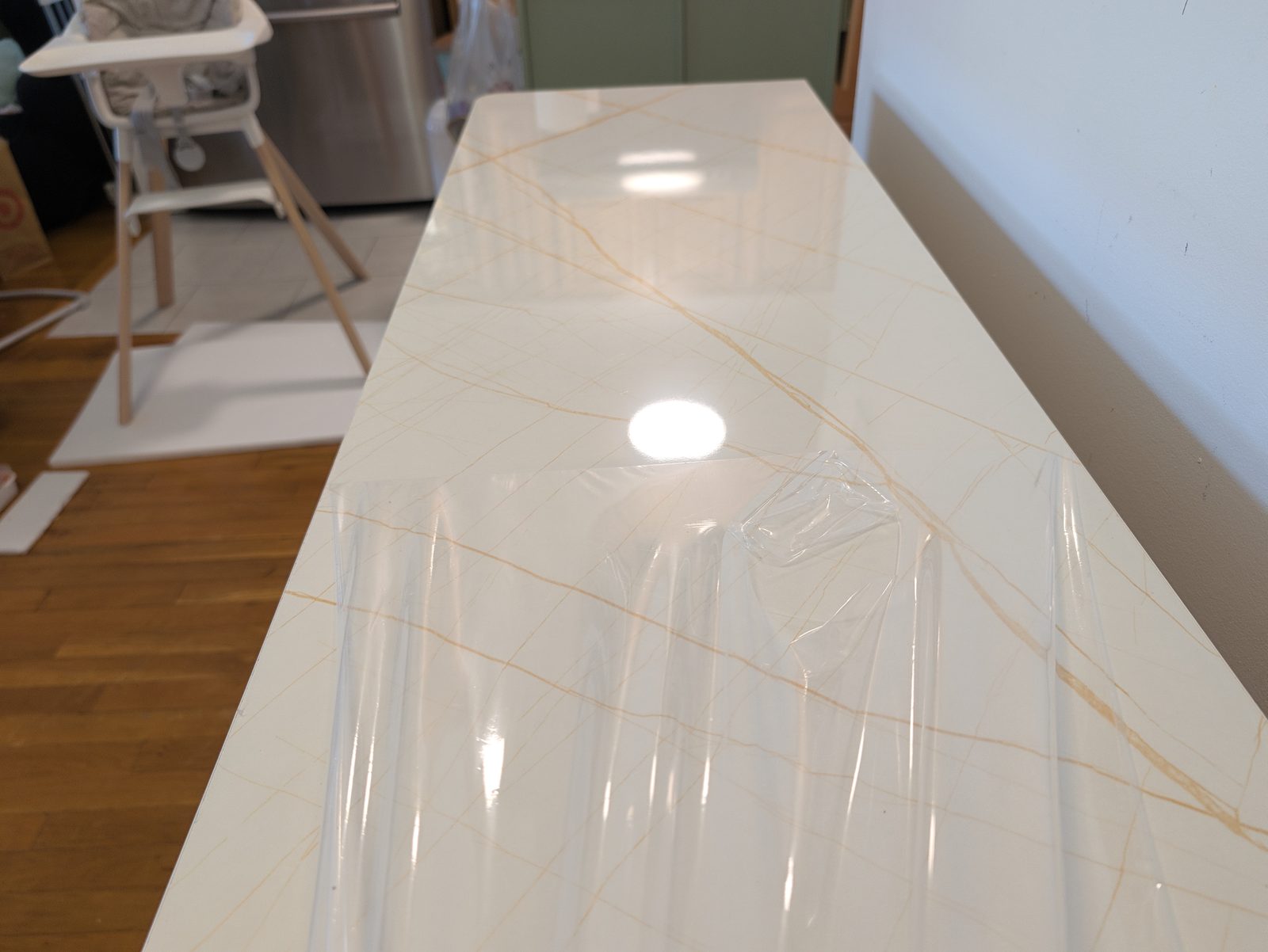 A glossy white marble-look cabinet top with thin gold veins, partly covered by a clear protective film