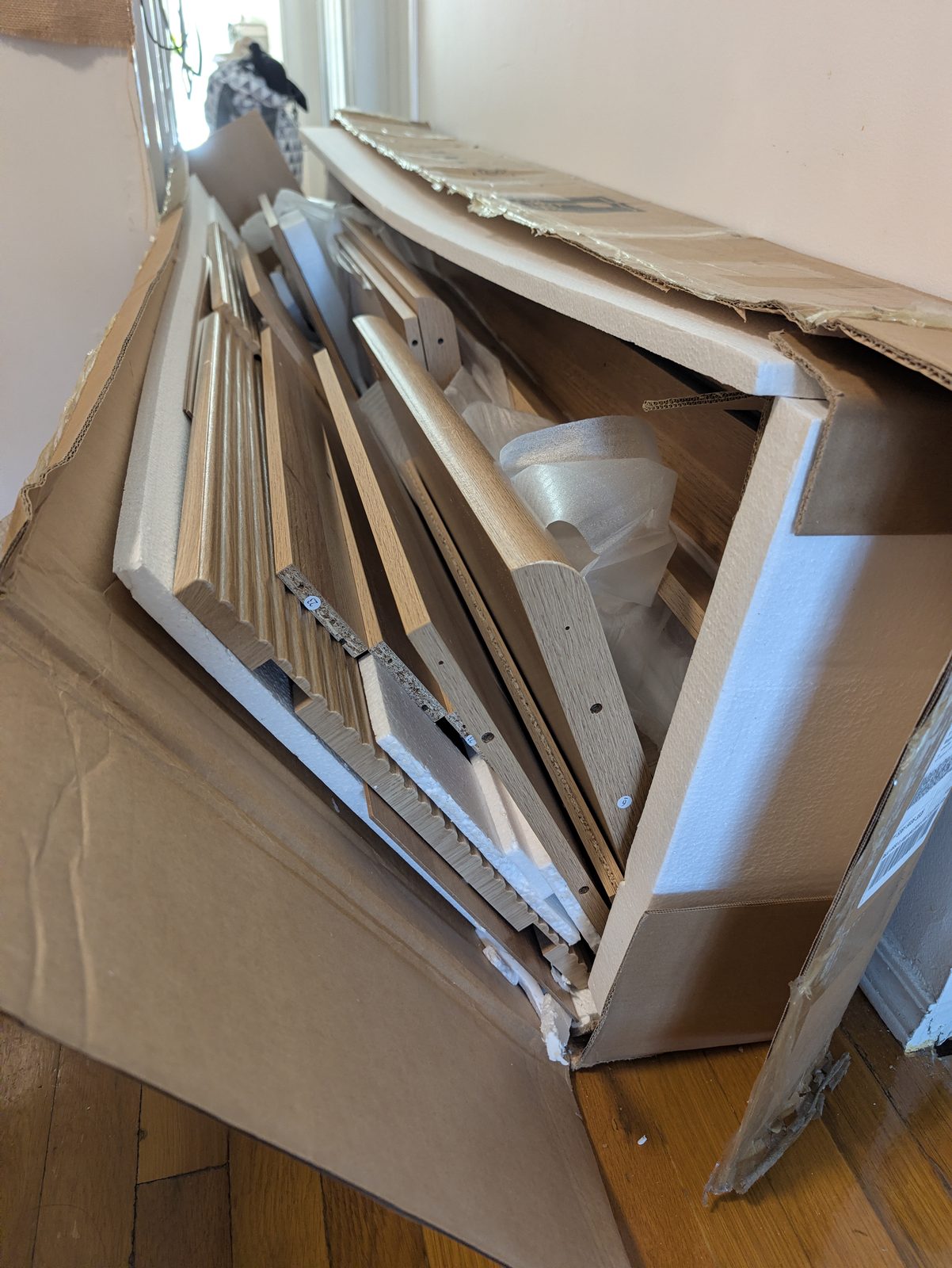 An opened cardboard box on its side with oak-look and fluted panels stacked inside white foam
