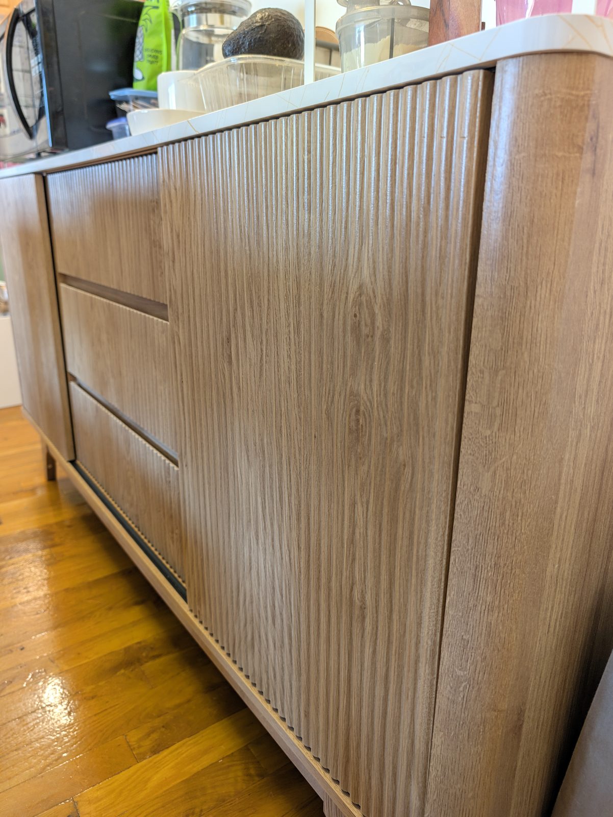 Close view of a light oak fluted sliding door and three fluted drawer fronts, with the cabinet's rounded side at the right