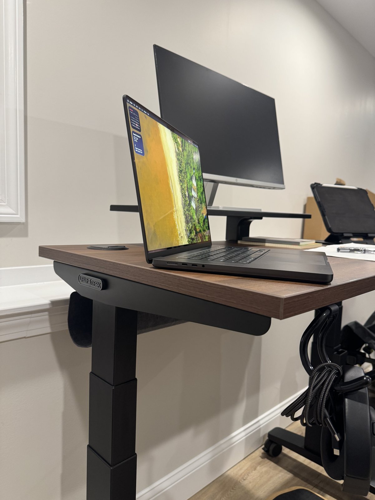 The left leg of an Uplift V3 desk under a walnut laminate top with a laptop on it