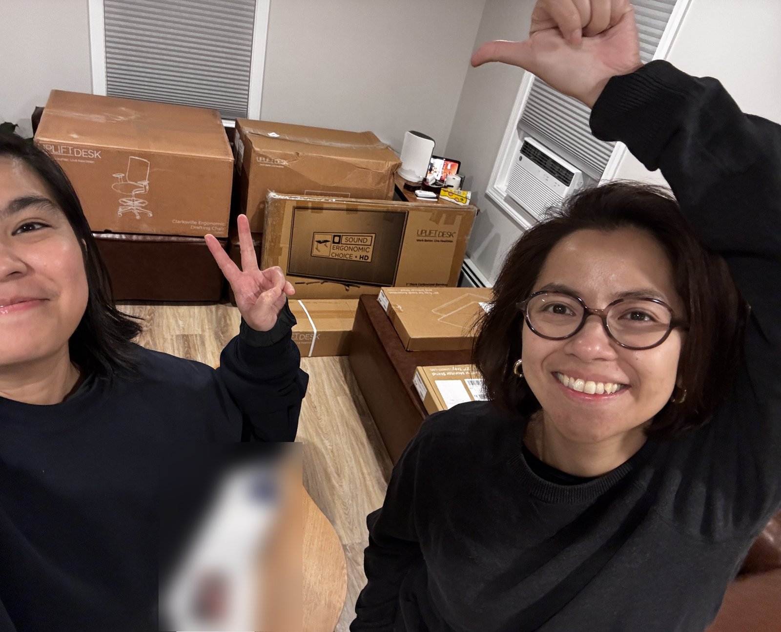 Uplift boxes in a room, including the Clarksville drafting chair's box and the desktop's box, with two people in front