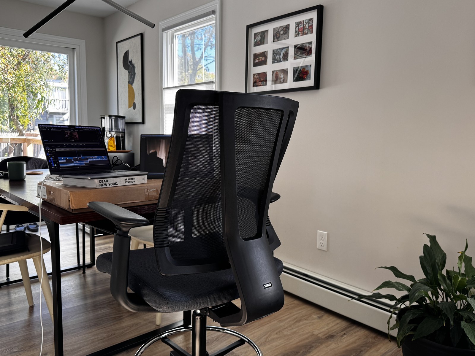 An Uplift Clarksville drafting chair pulled up to a dining table, with a laptop raised on a book on top of a box